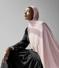 Woman wearing a light pink hijab and black outfit against a gray background