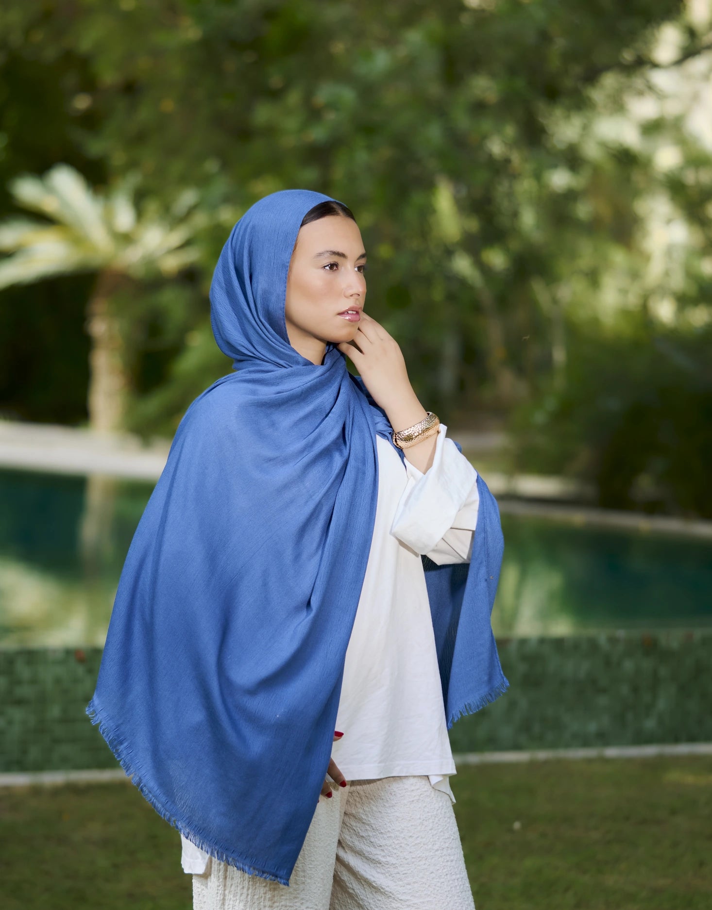 Woman wearing a blue hijab outdoors with greenery in the background