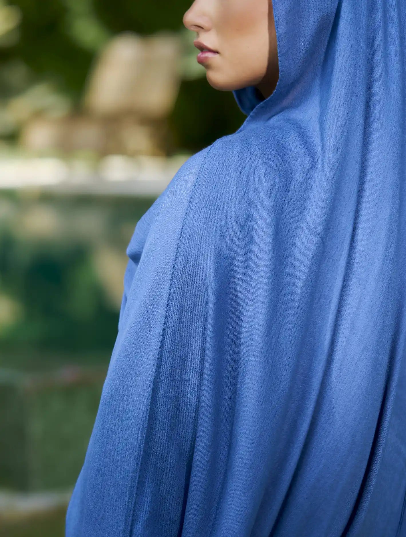 Person wearing a blue hooded garment with a blurred natural background