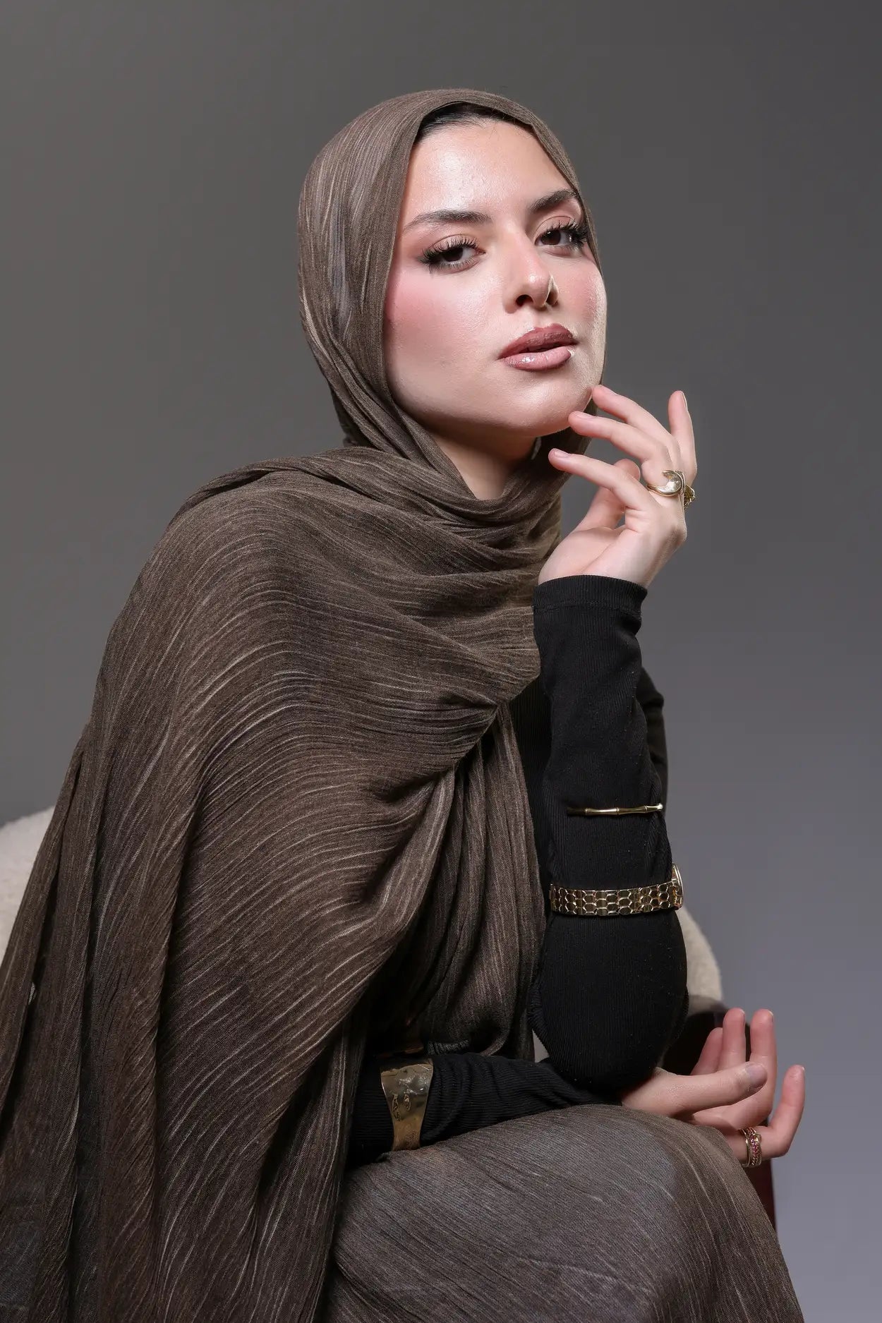 Woman wearing a brown hijab and black outfit against a gray background