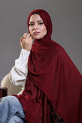 Woman wearing a red hijab and white shirt against a gray background