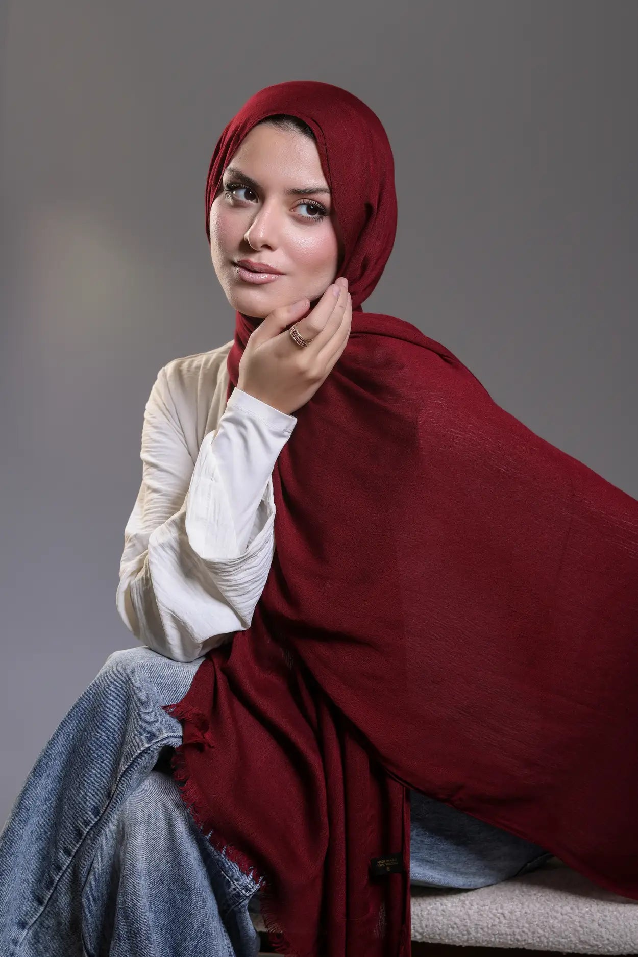 Woman wearing a red hijab and white shirt against a gray background
