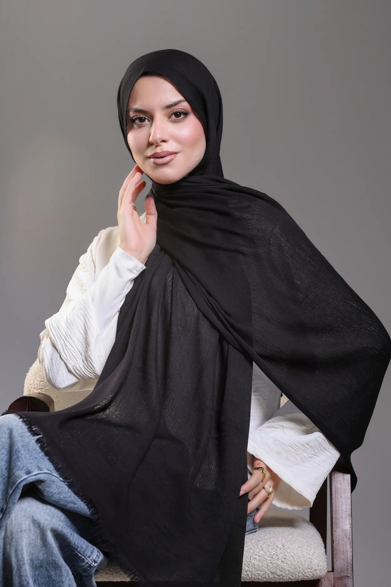 Woman wearing a black hijab and white top against a gray background