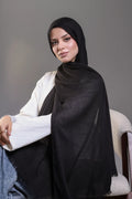 Woman wearing a black hijab and white sweater against a gray background