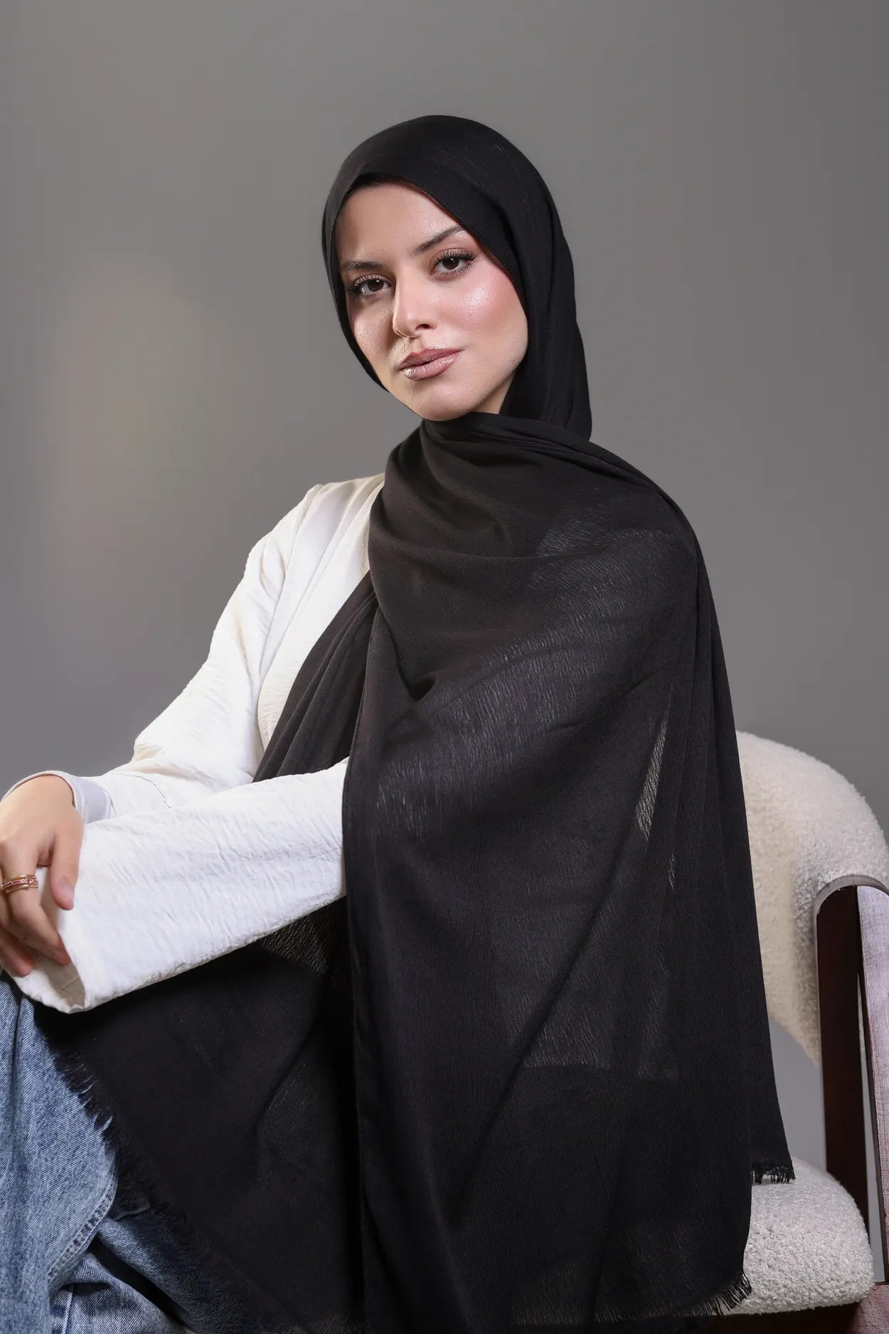 Woman wearing a black hijab and white sweater against a gray background