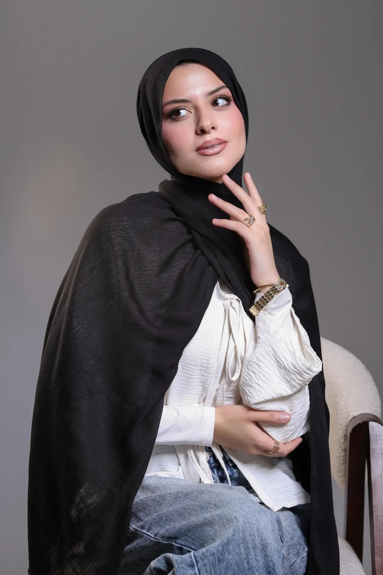 Woman wearing a black hijab and white top with a gray background