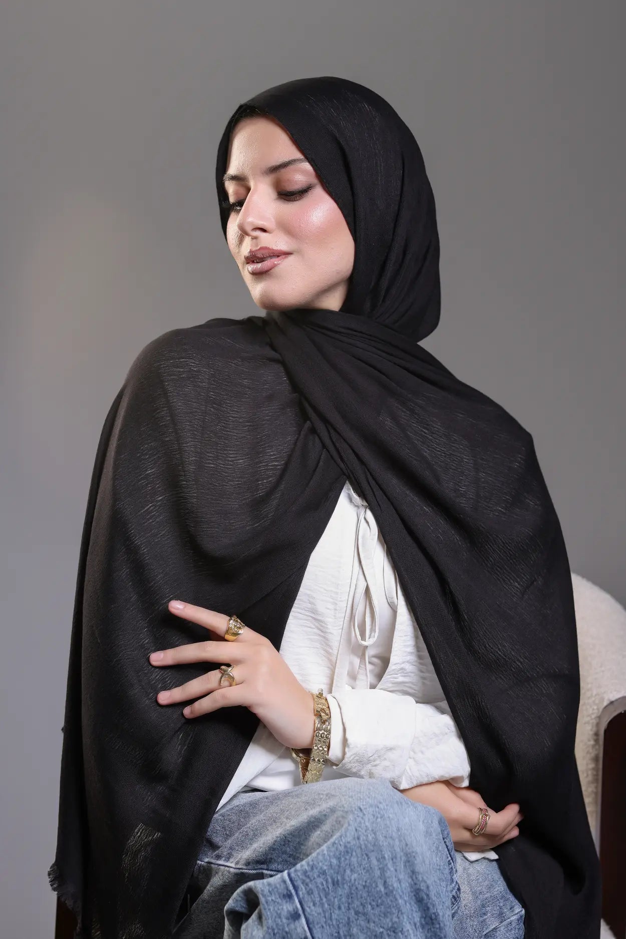 Woman wearing a black hijab and white top against a gray background