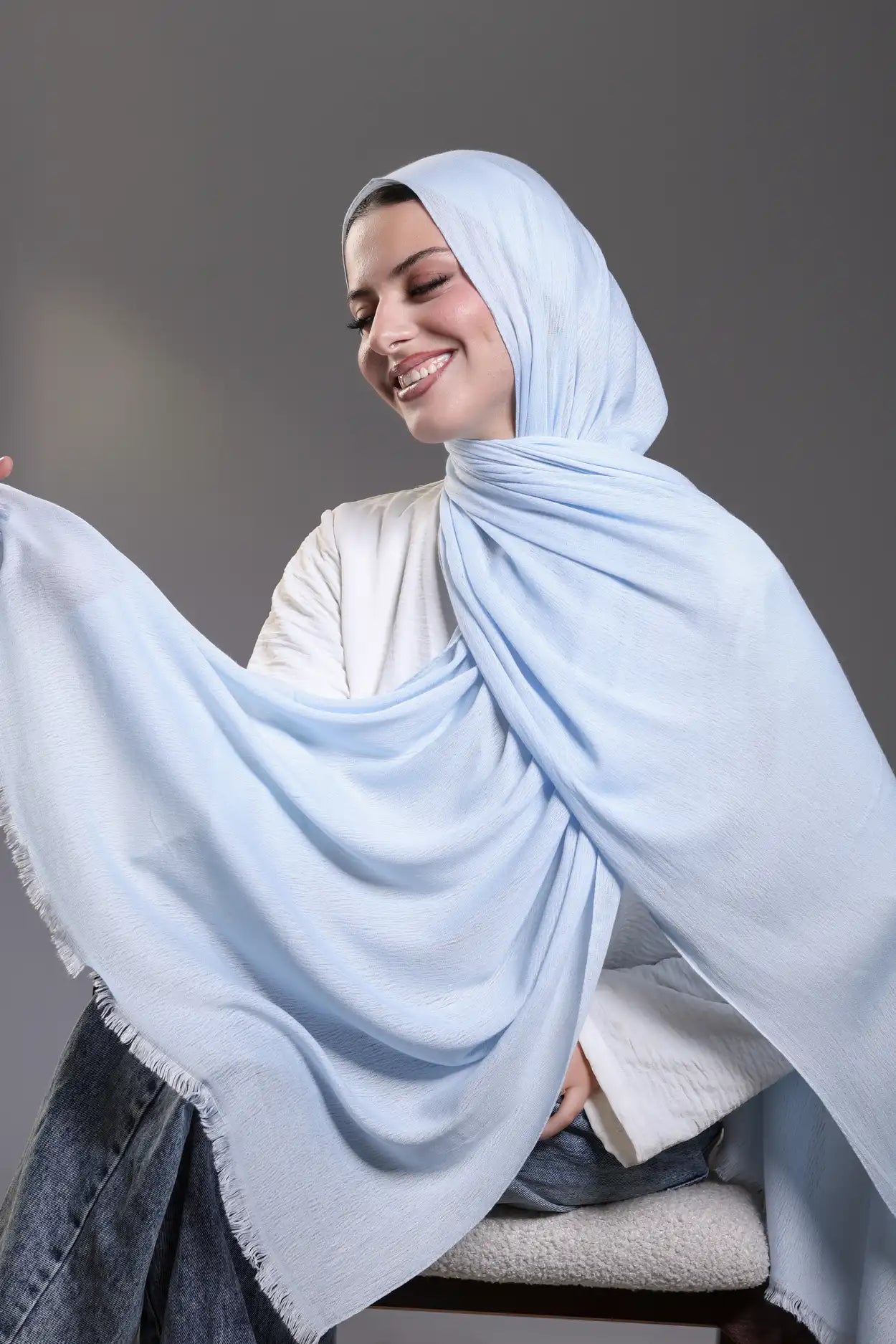 Woman wearing a light blue hijab against a gray background