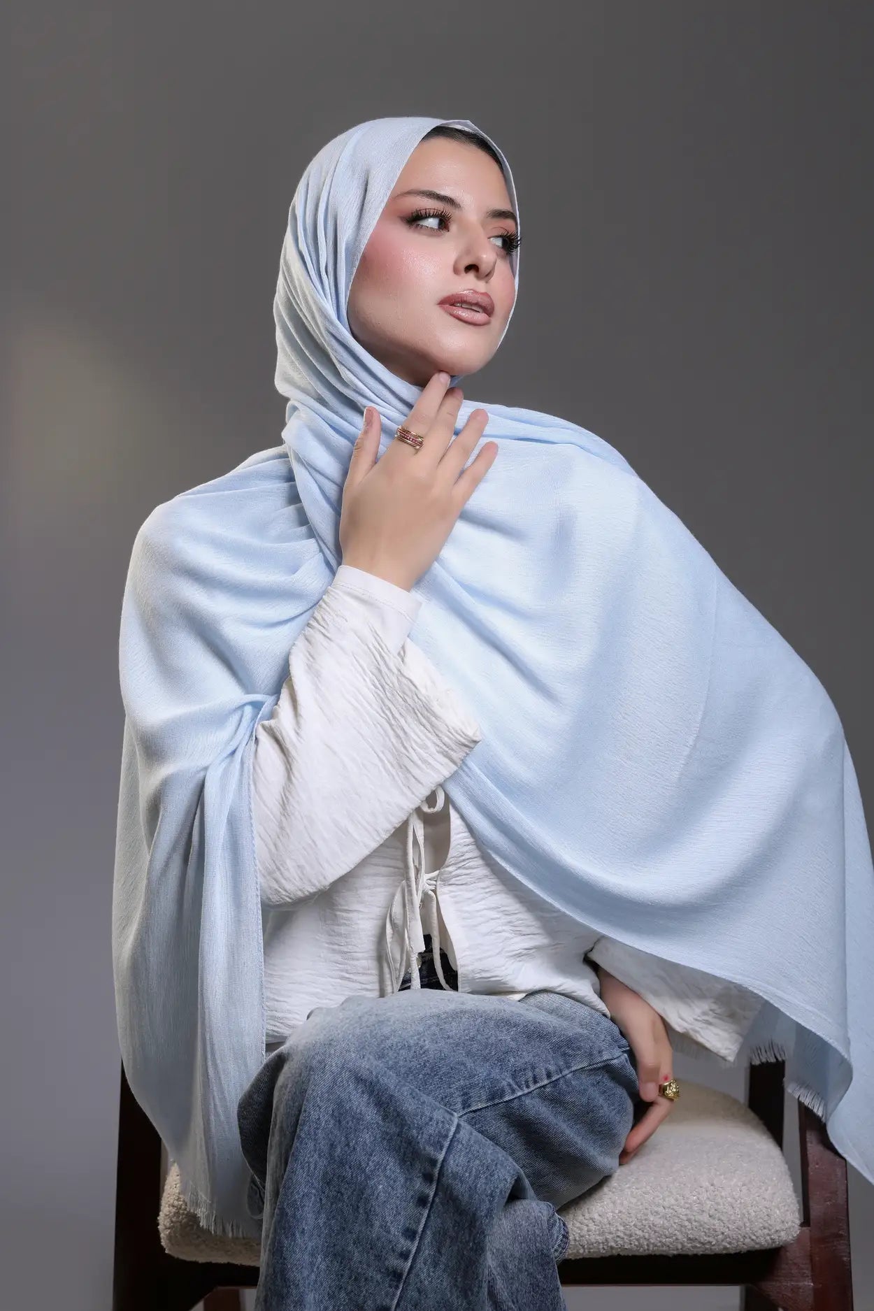 Woman wearing a light blue hijab and white sweater against a gray background