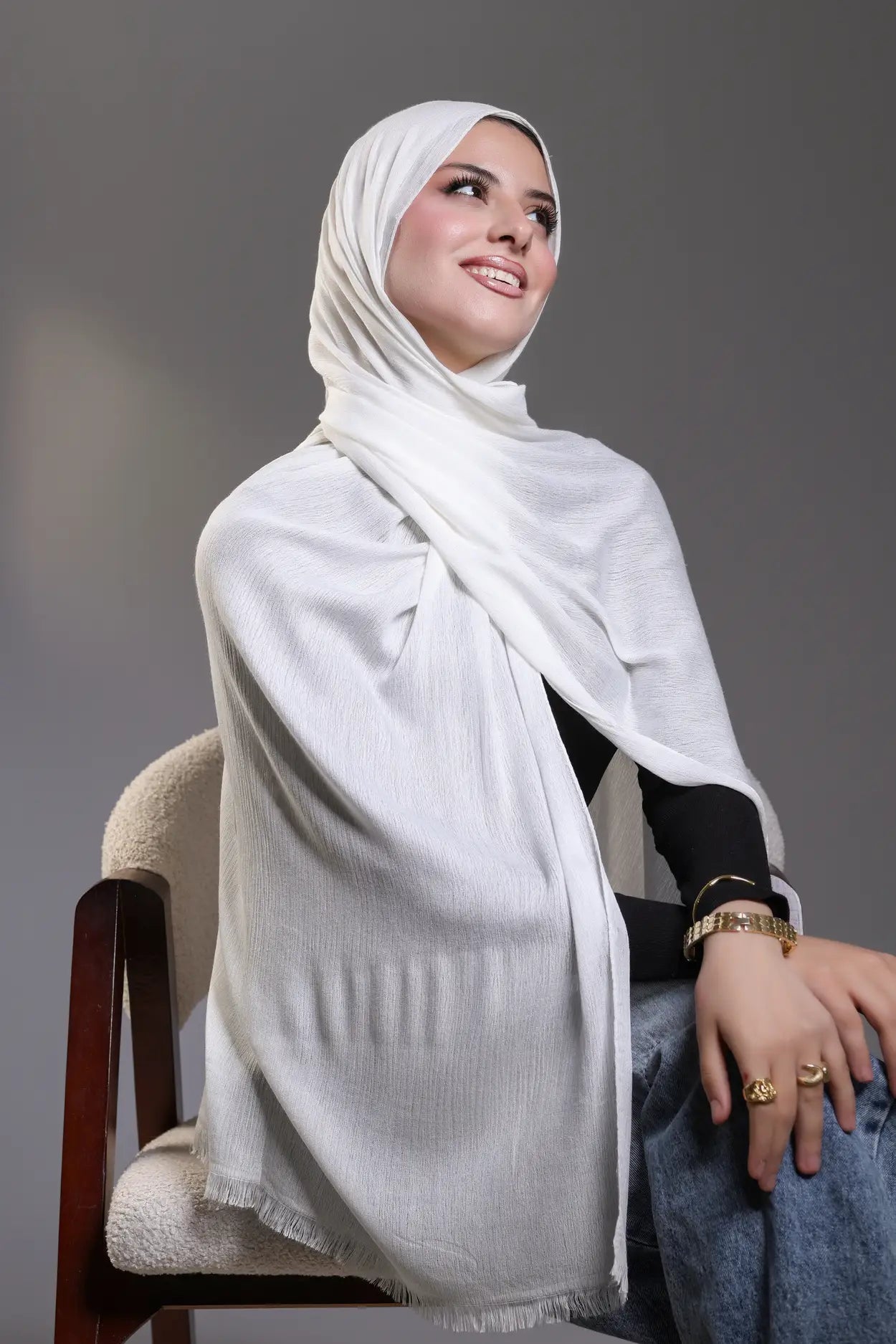Woman wearing a white hijab sitting on a chair against a gray background