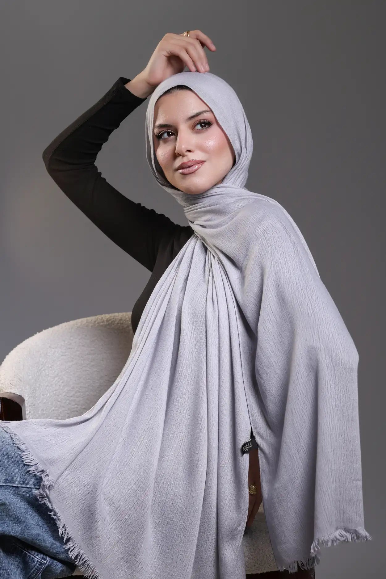 Woman wearing a light gray hijab against a gray background