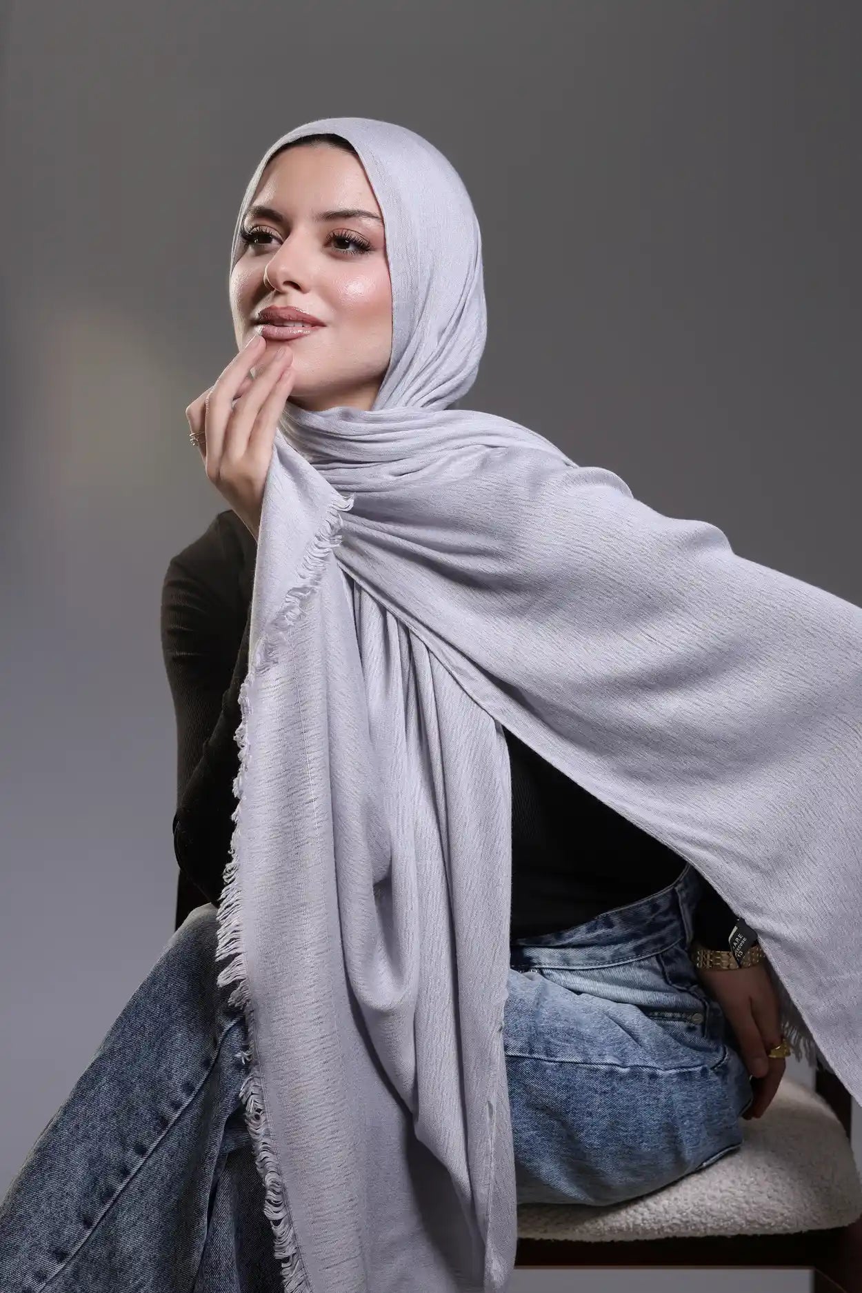 Woman wearing a light gray hijab against a gray background