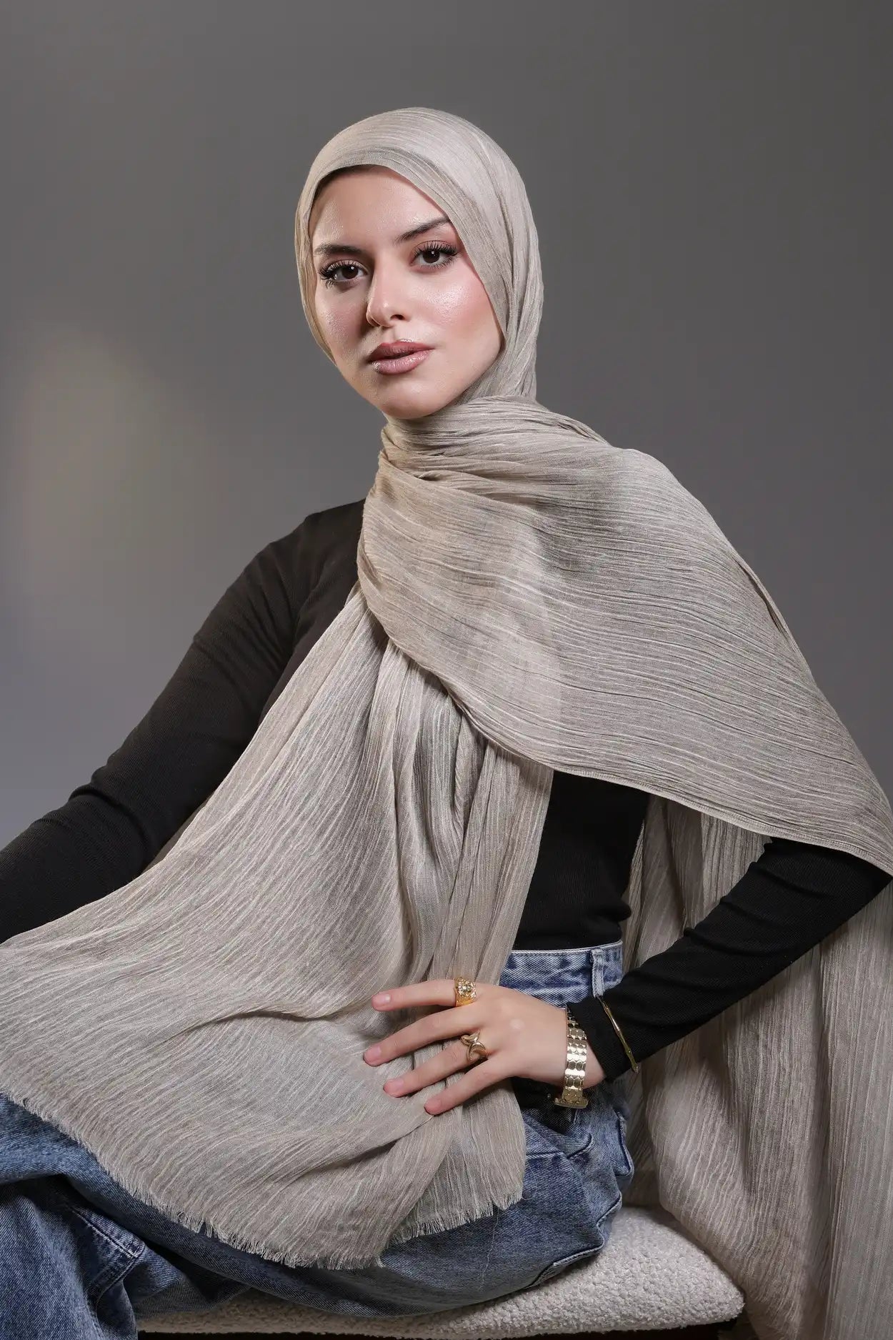 Woman wearing a beige hijab and scarf against a gray background