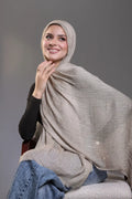 Woman wearing a beige hijab and sitting on a chair against a gray background