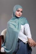 Woman wearing a light blue hijab and white shirt against a gray background