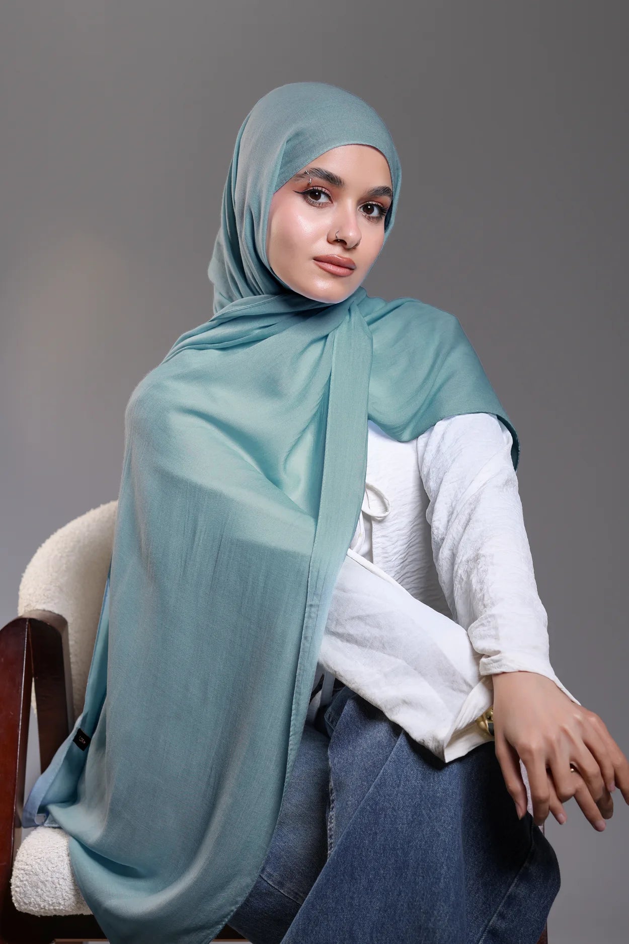 Woman wearing a light blue hijab and white shirt against a gray background