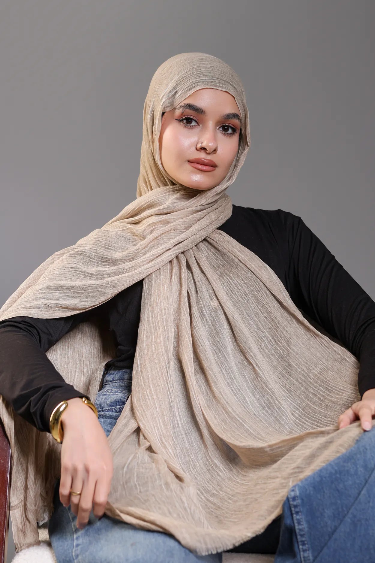 Woman wearing a beige hijab against a gray background