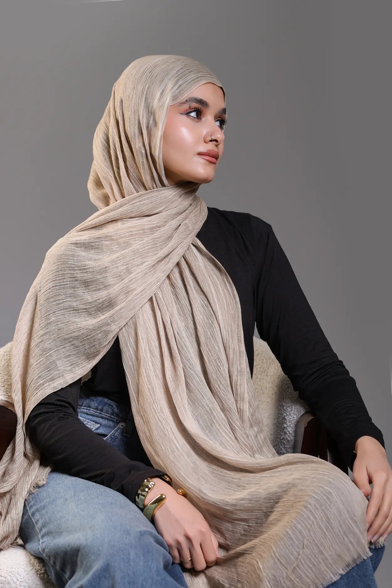 Woman wearing a beige hijab and black top against a gray background