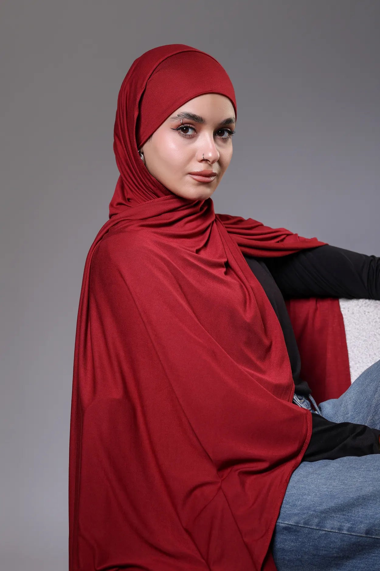 Woman wearing a red hijab against a gray background