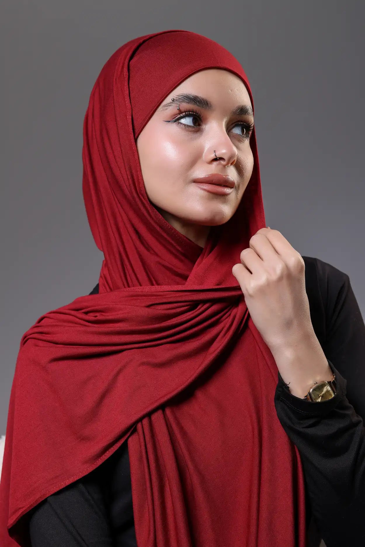 Woman wearing a red hijab against a gray background