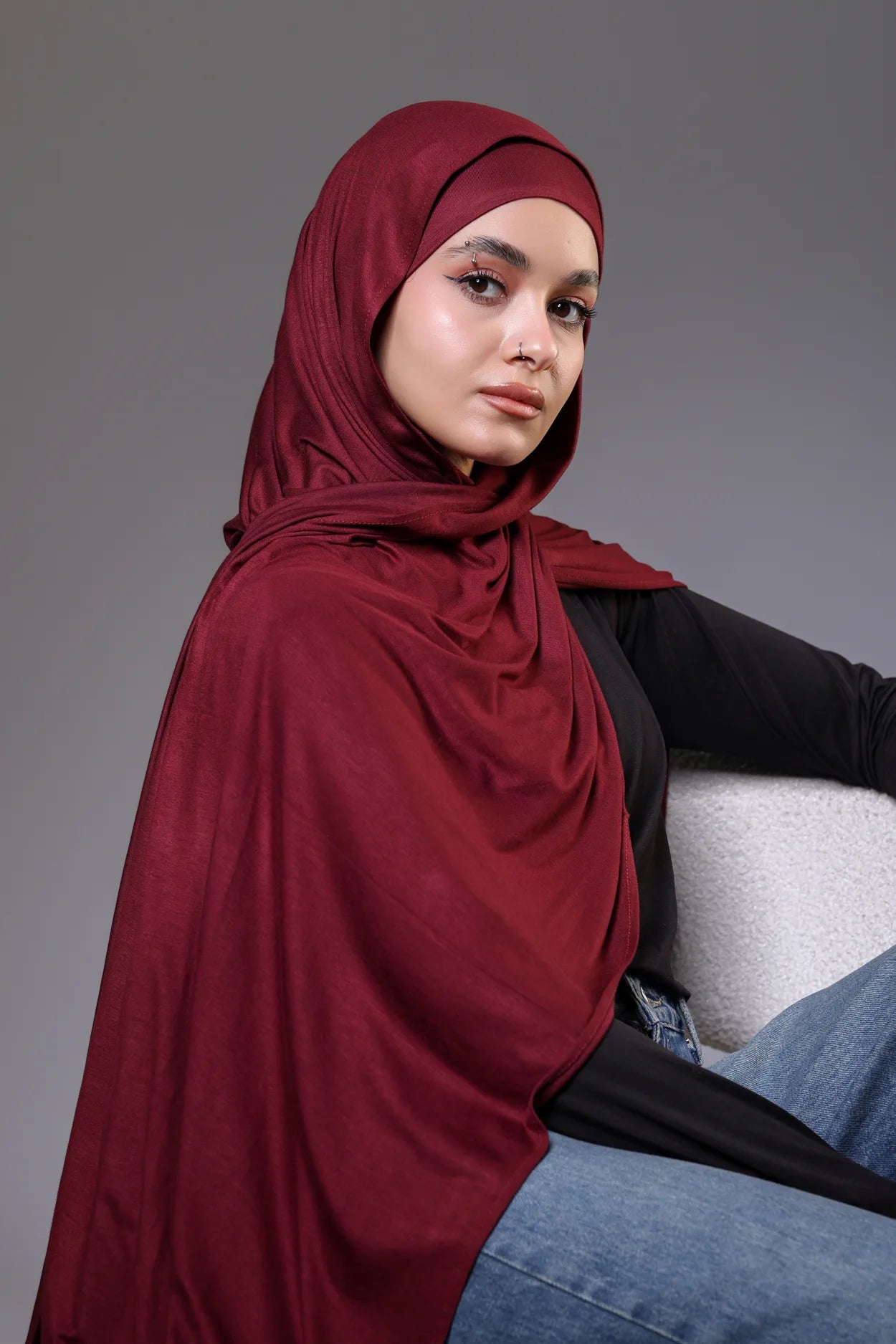 Woman wearing a red hijab sitting on a gray couch against a gray background