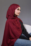 Woman wearing a red hijab sitting on a gray background