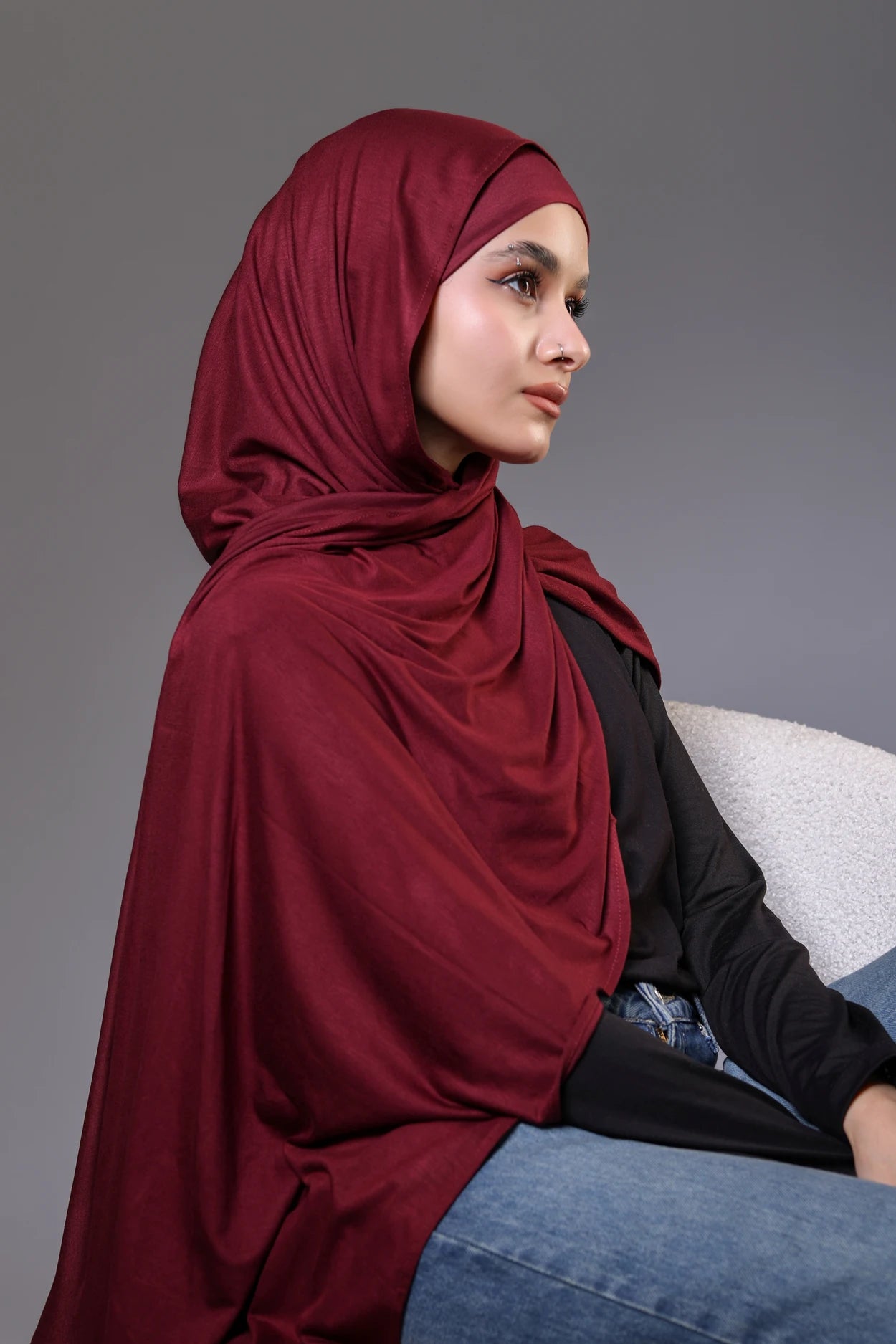 Woman wearing a red hijab sitting on a gray background