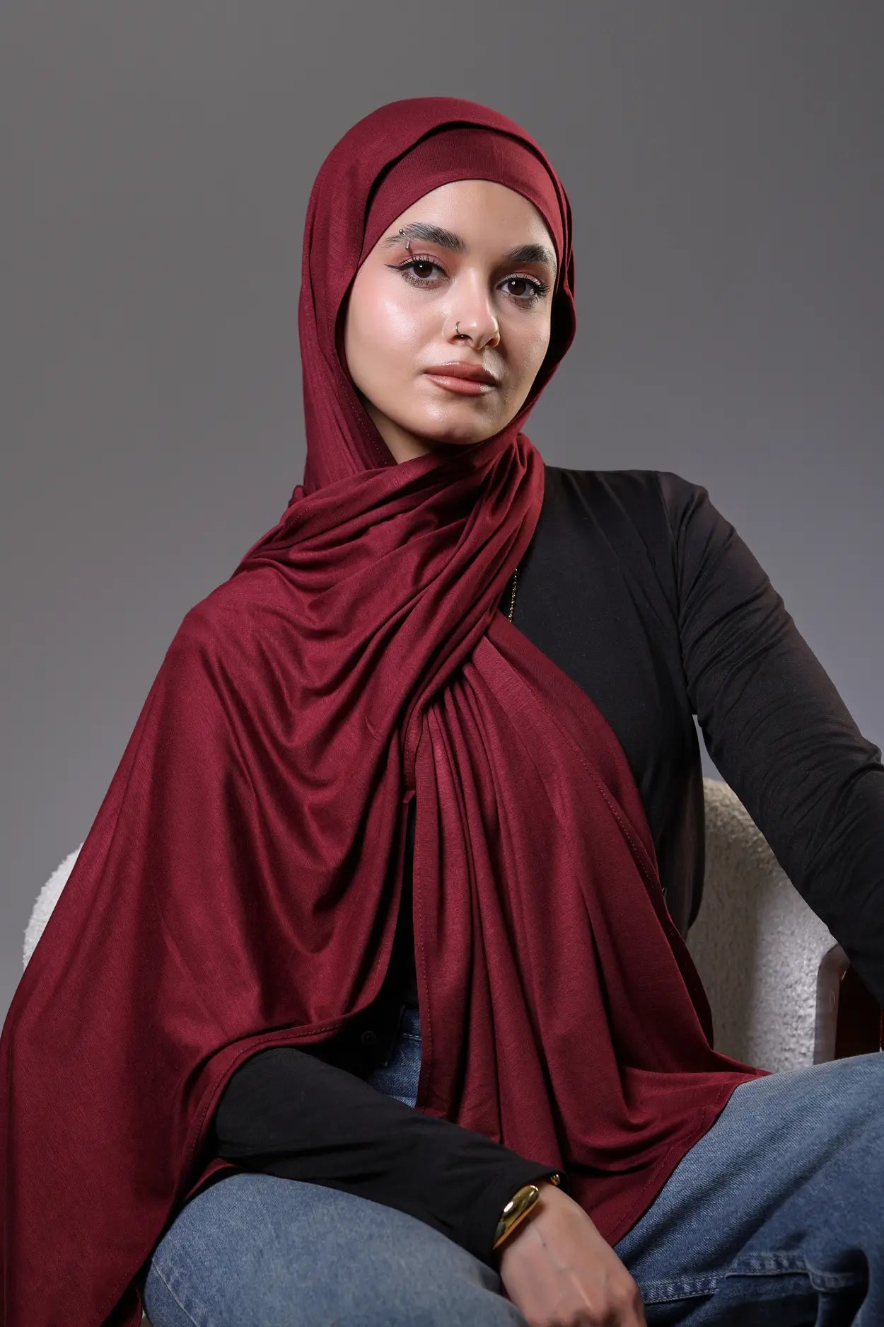 Woman wearing a red hijab and black top against a gray background