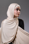Woman wearing a beige hijab against a gray background