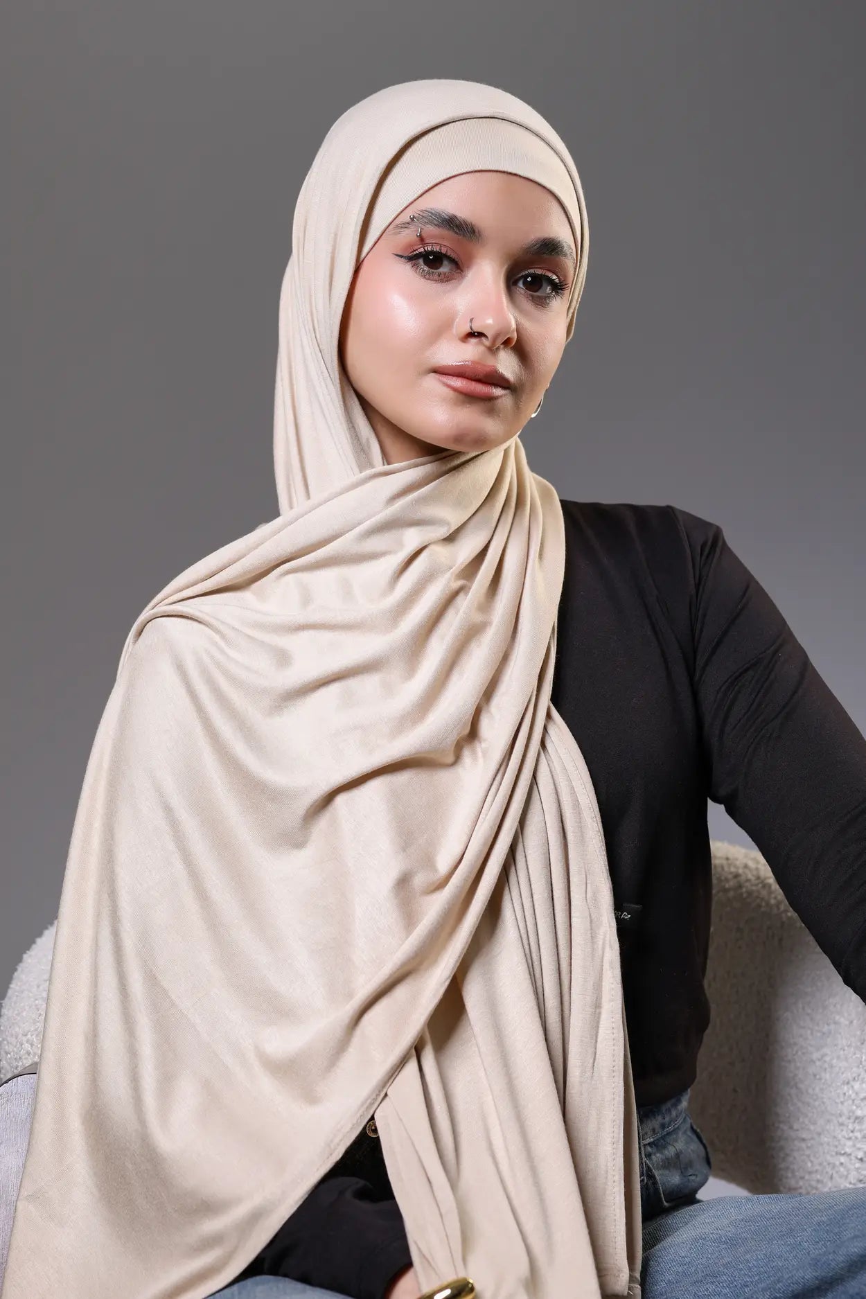Woman wearing a beige hijab and black top on a gray background