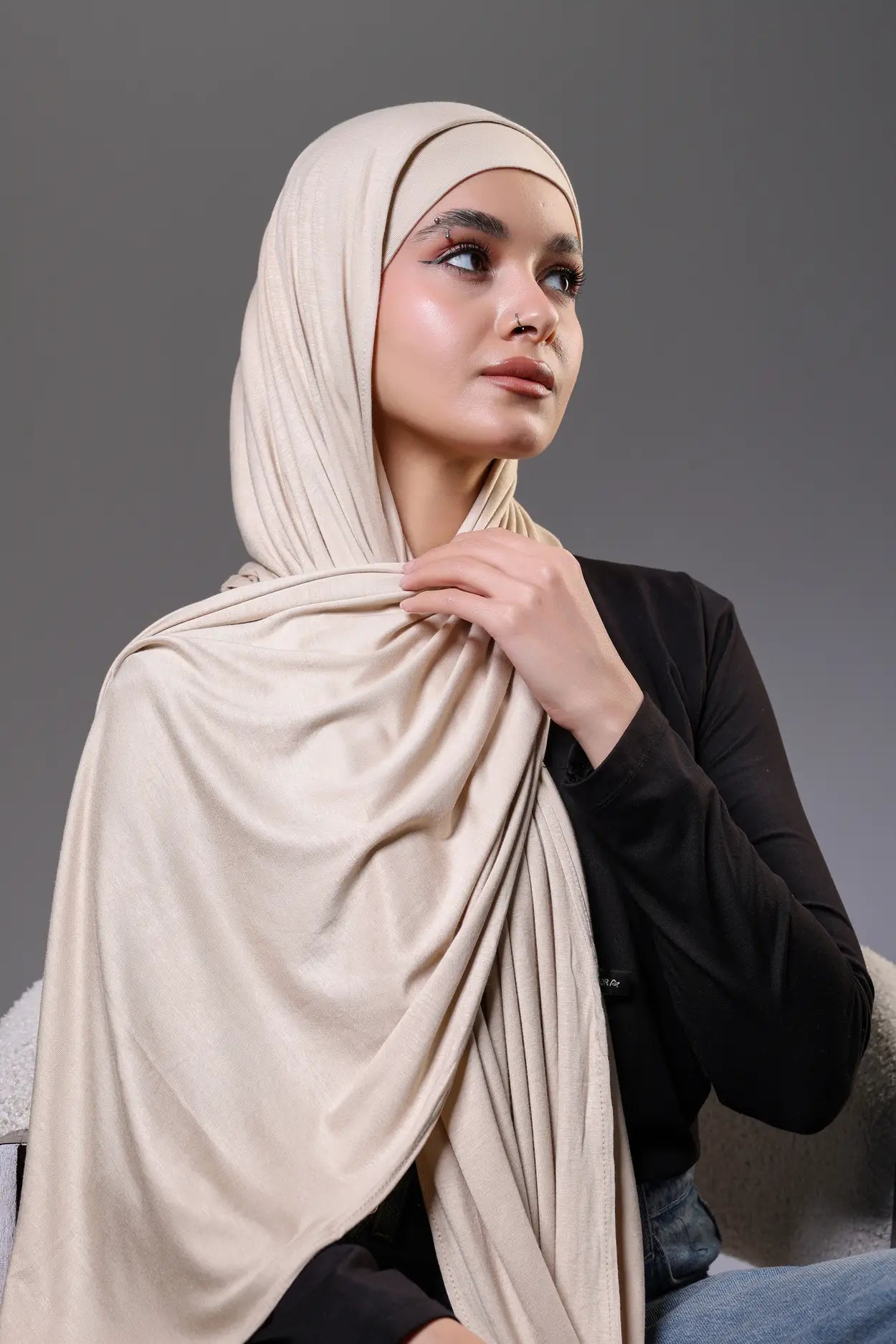 Woman wearing a beige hijab against a gray background