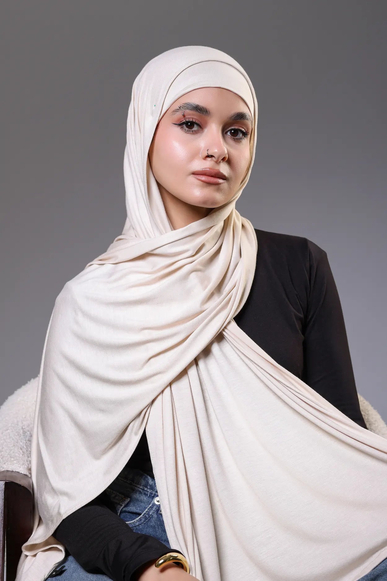 Woman wearing a beige hijab against a gray background