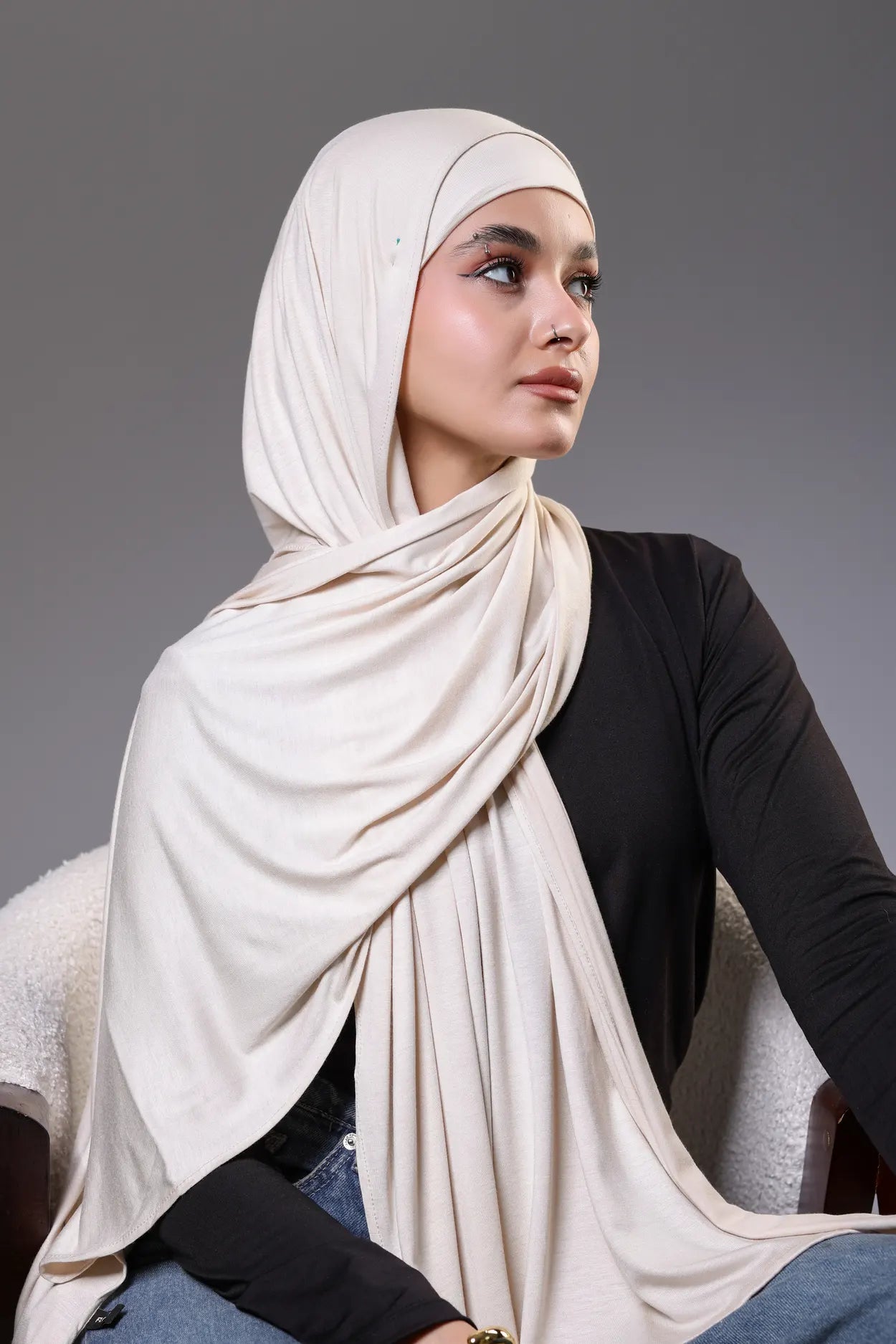 Woman wearing a beige hijab against a gray background