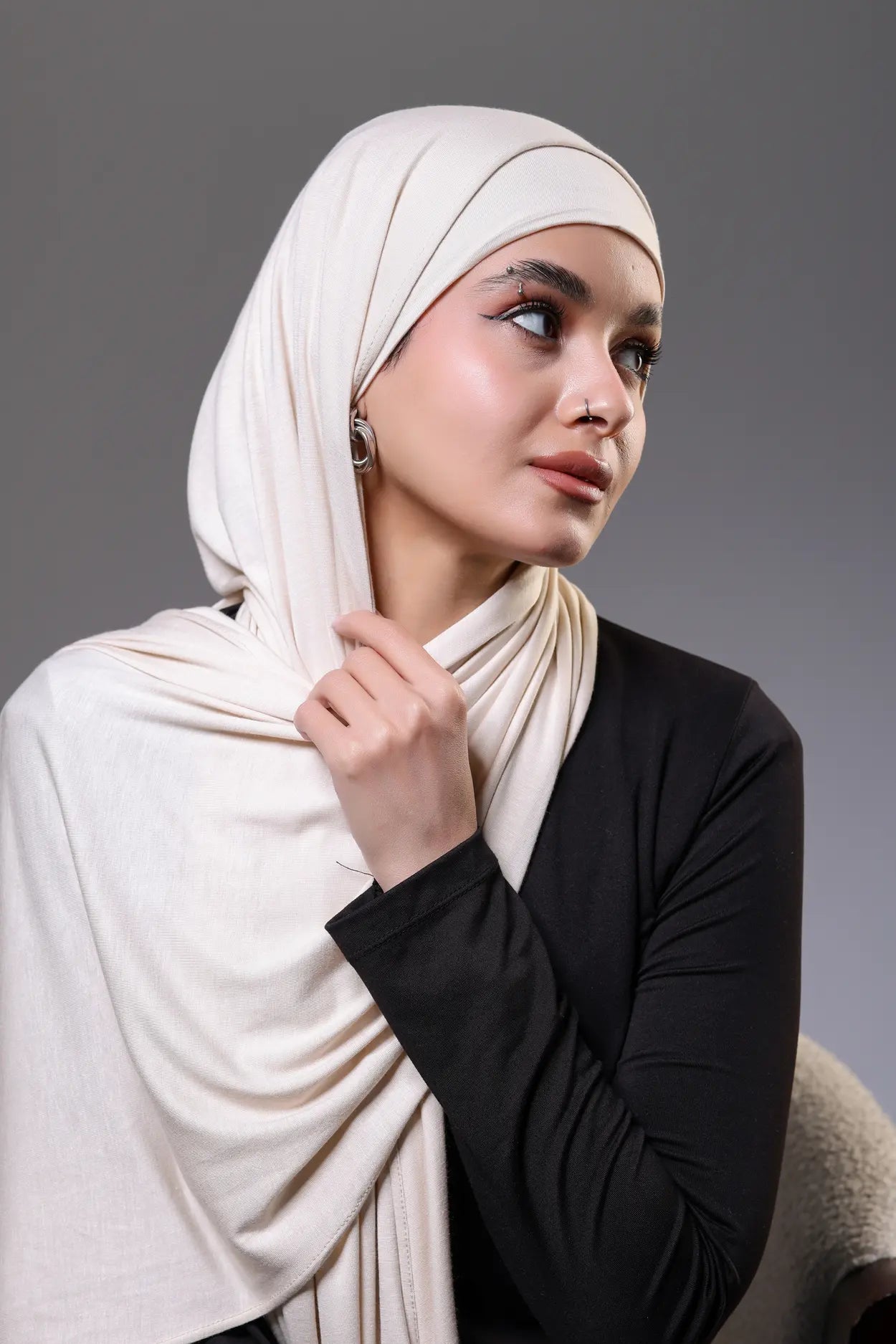 Woman wearing a Beige  hijab and black top against a gray background