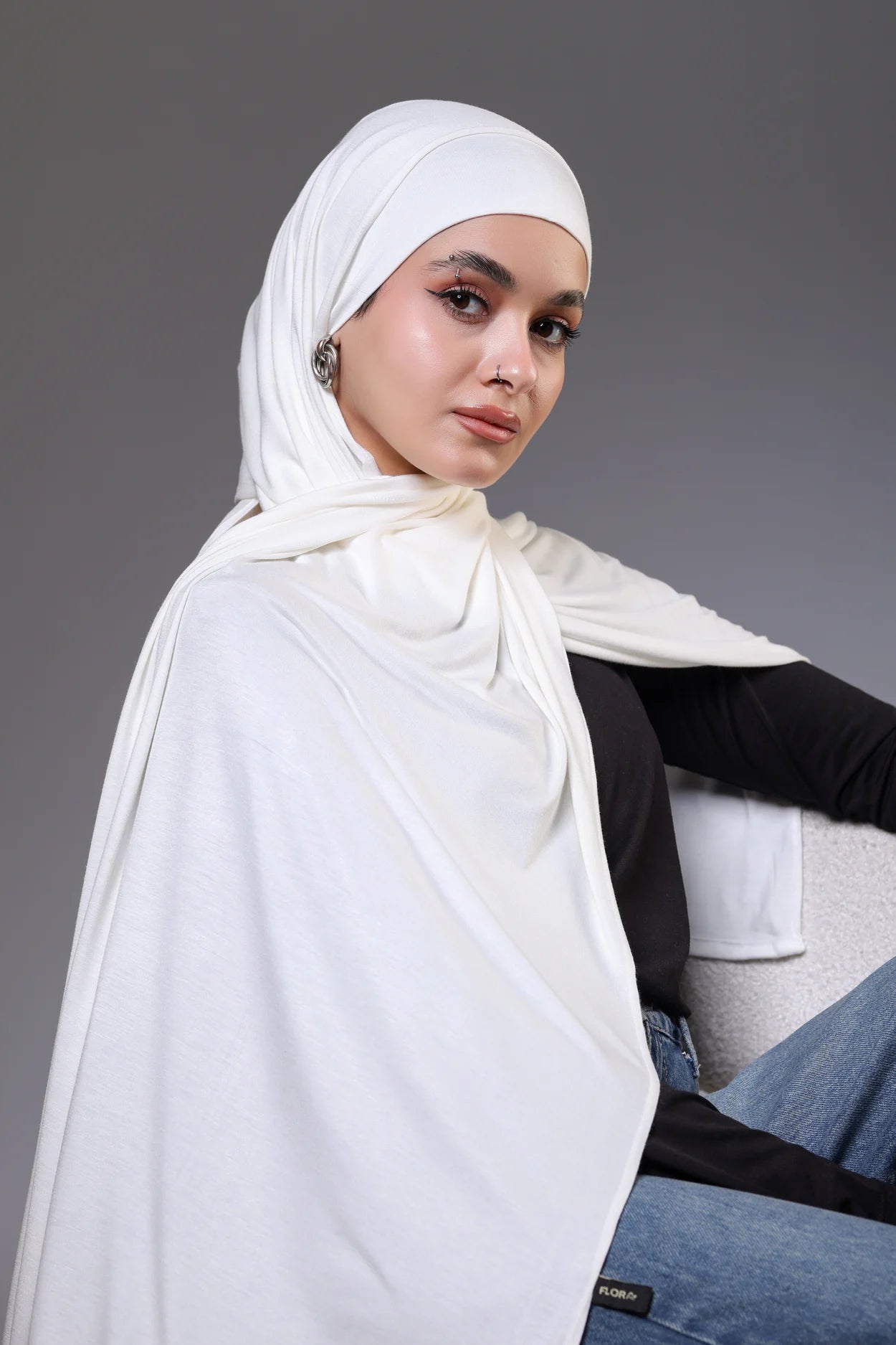 Woman wearing a white hijab against a gray background