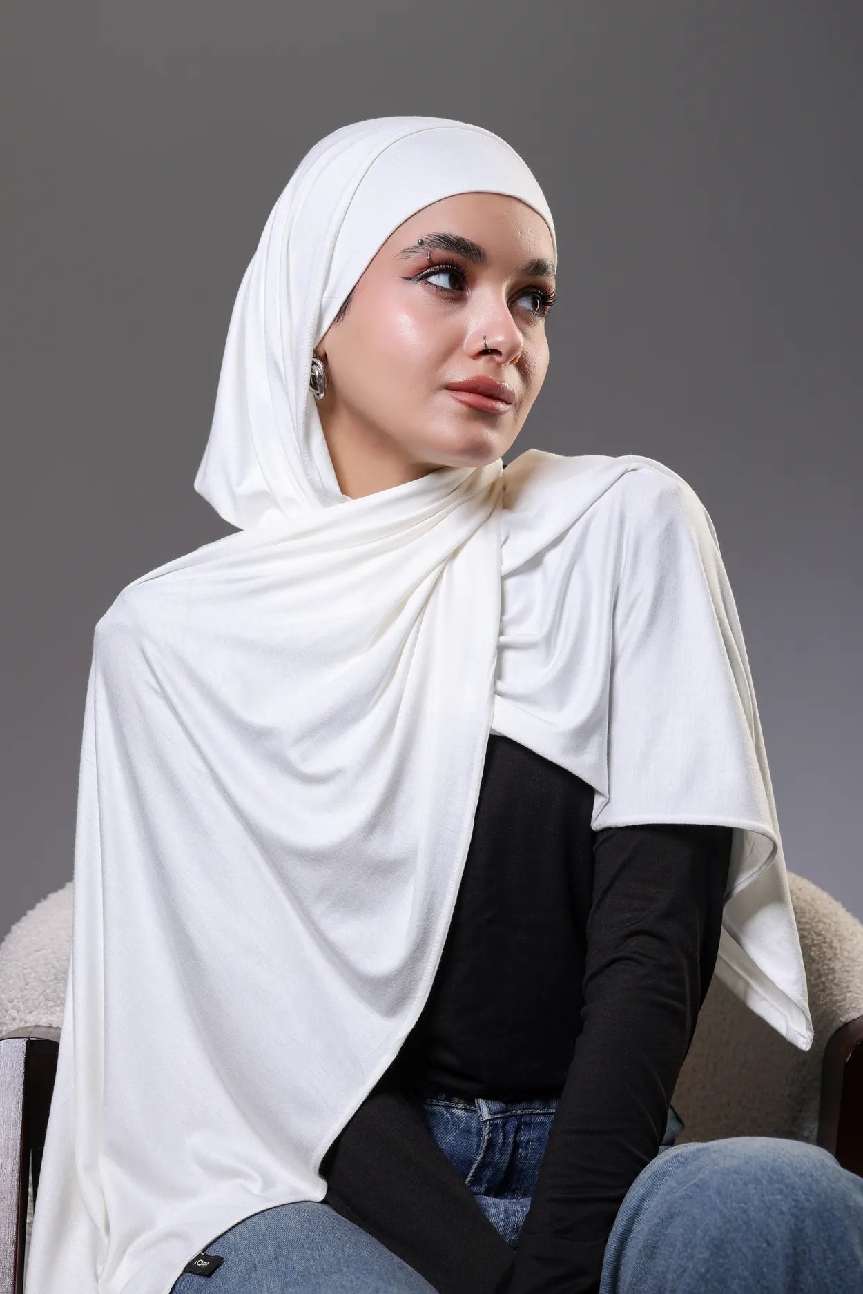 Woman wearing a white hijab and black top against a gray background