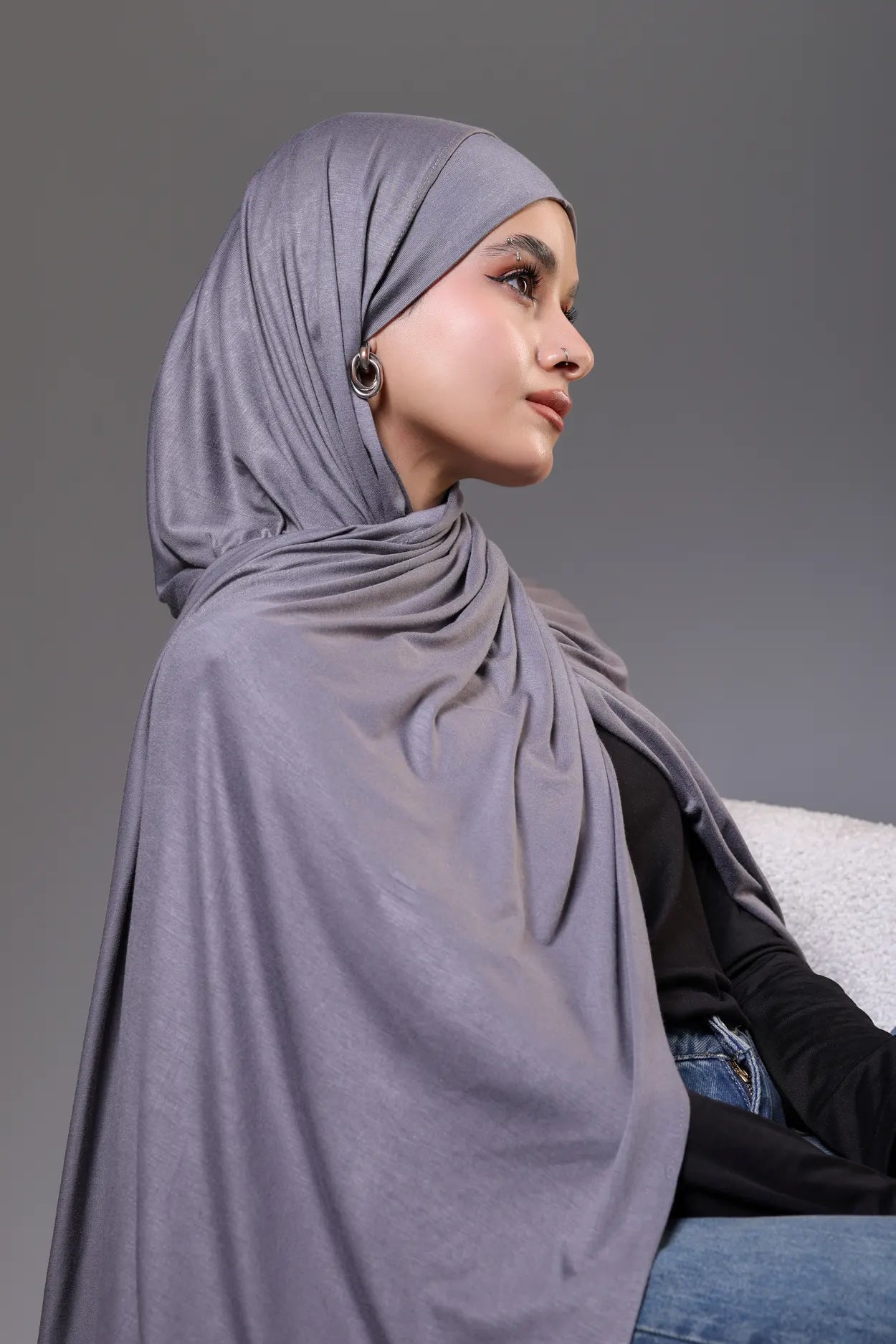 Woman wearing a gray hijab sitting against a gray background