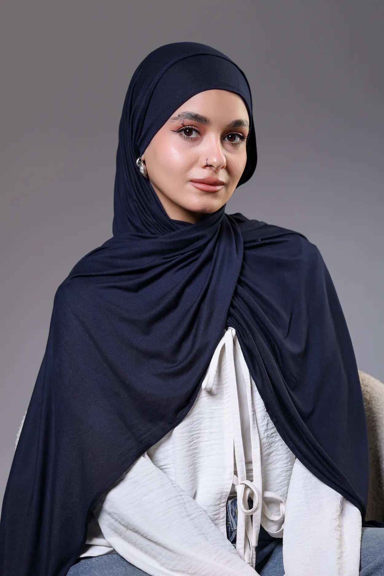 Woman wearing a navy hijab and white top against a gray background