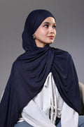Woman wearing a navy hijab and white top against a gray background