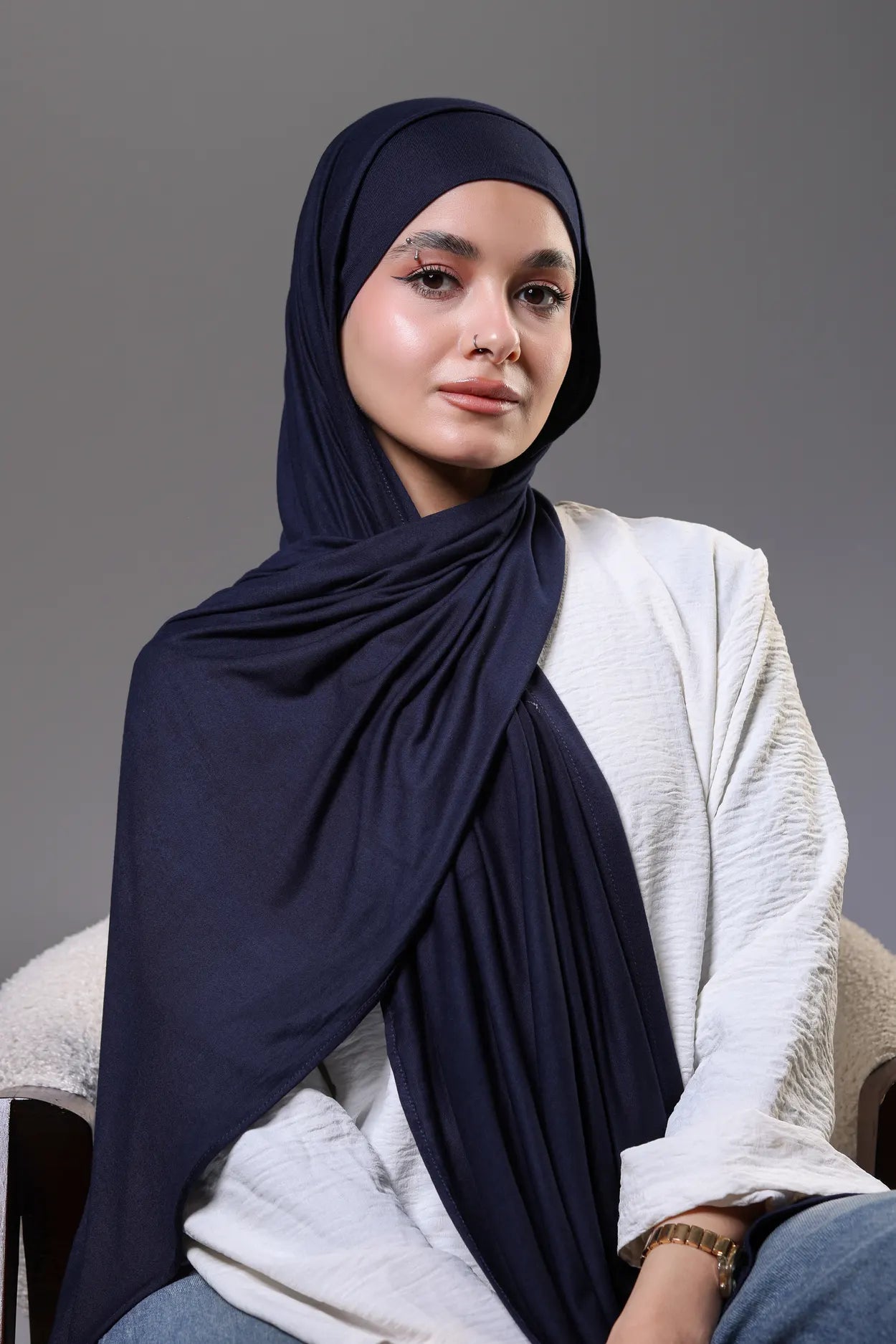Woman wearing a navy hijab and white top against a gray background