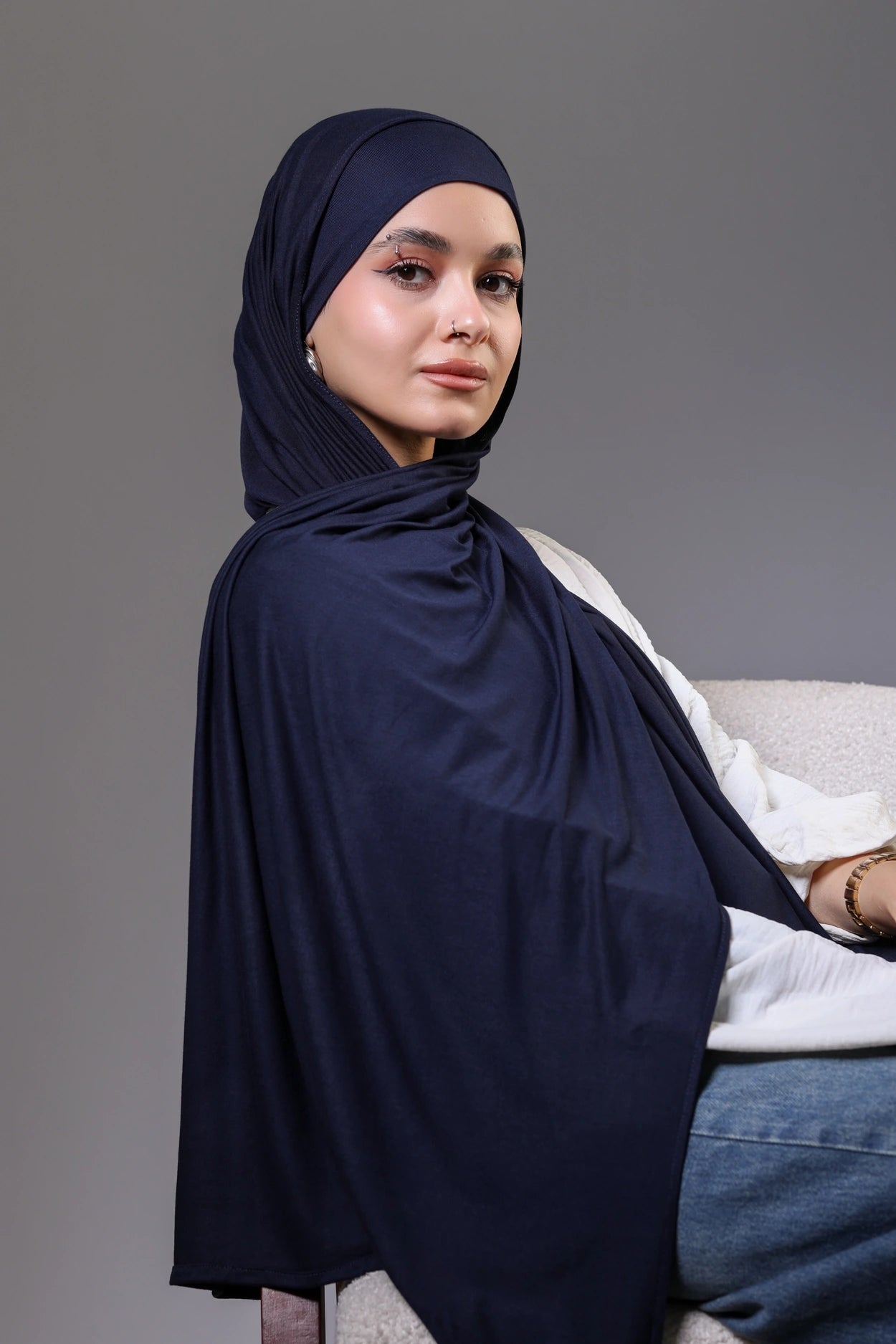 Woman wearing a navy hijab sitting on a gray background