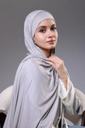 Woman wearing a light gray hijab against a gray background