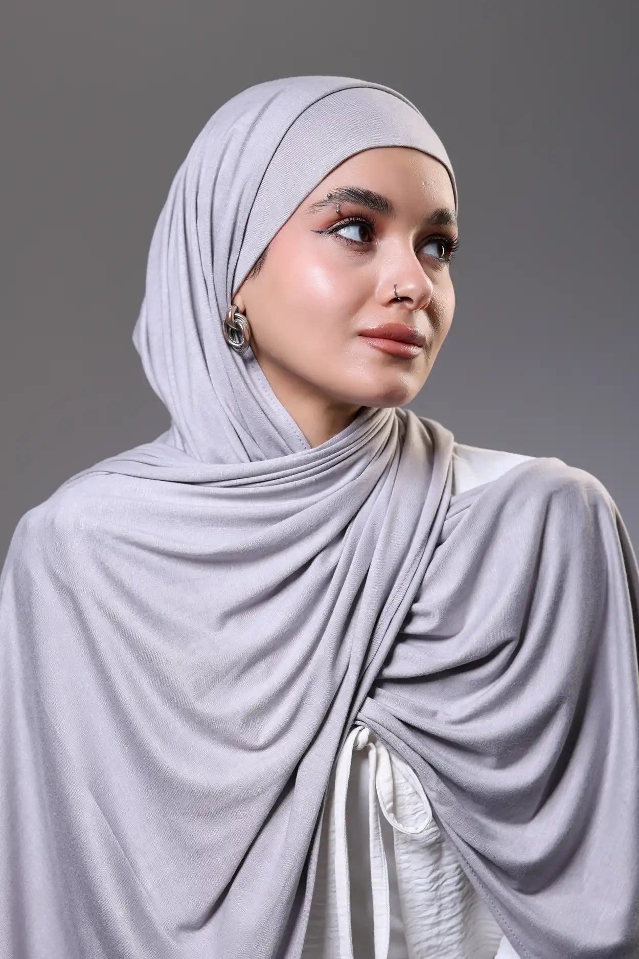 Woman wearing a light gray hijab against a gray background