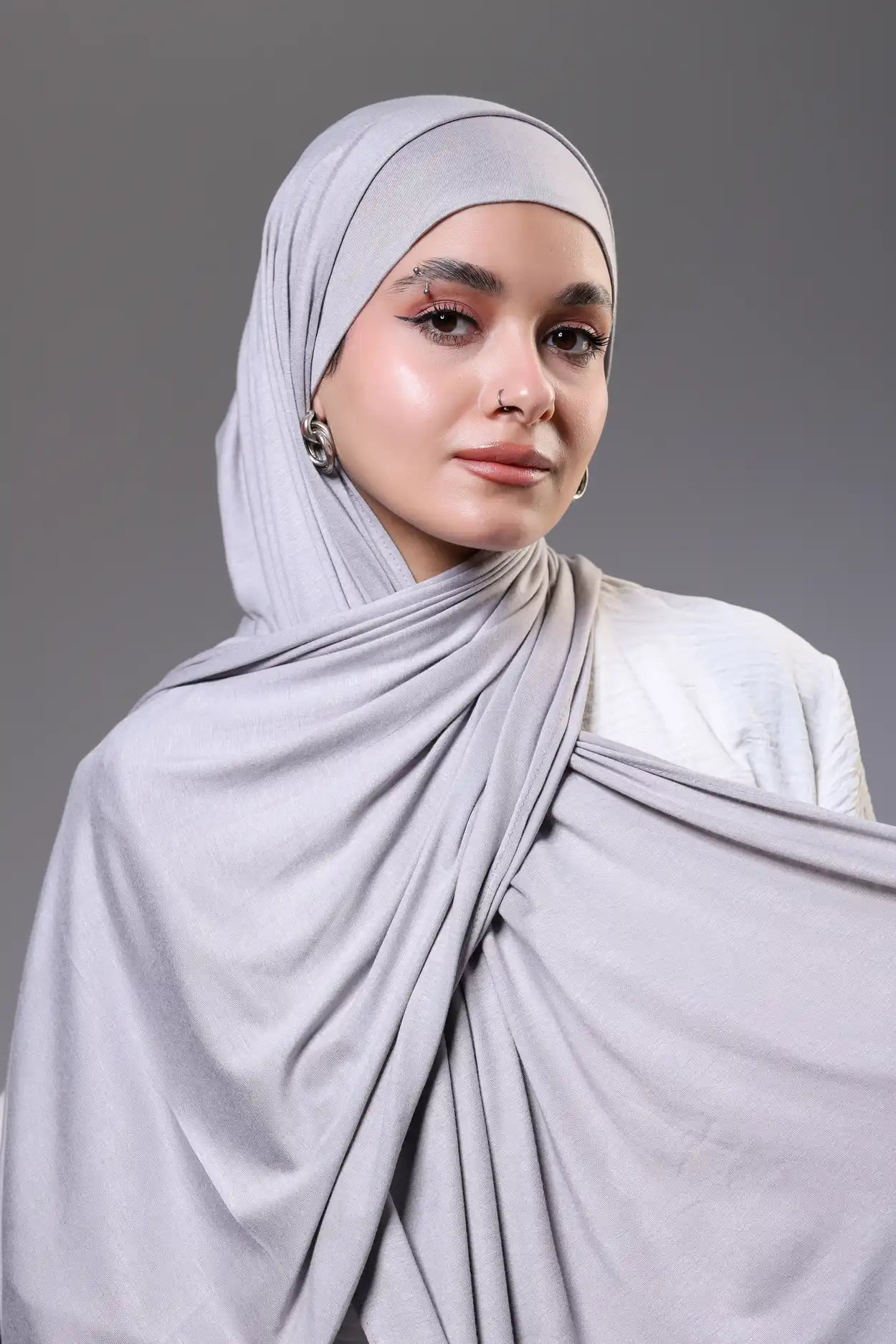 Woman wearing a light gray hijab against a gray background