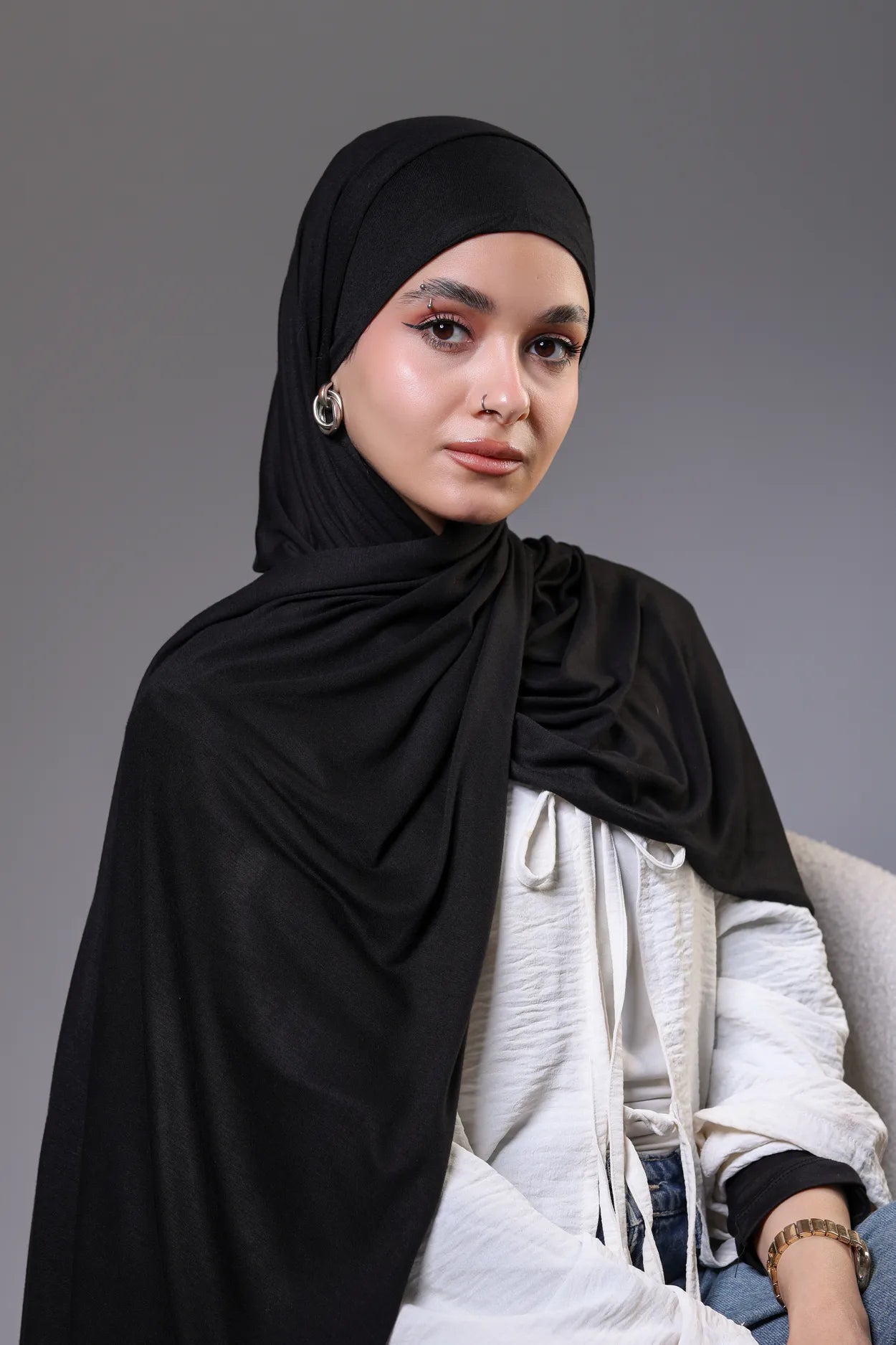 Woman wearing a black hijab and white shirt against a gray background