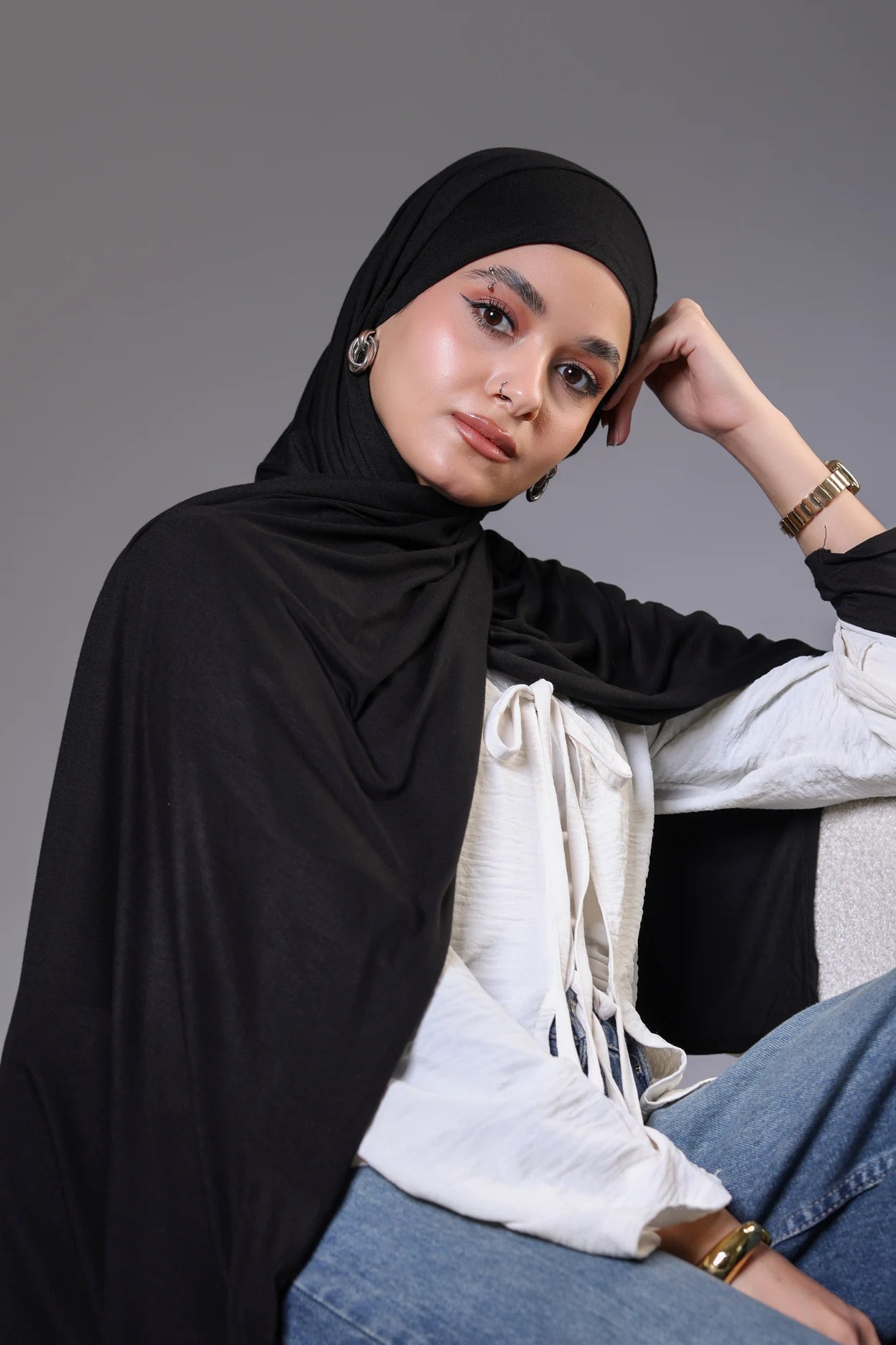 Woman wearing a black hijab and white top with a gray background