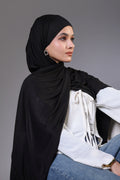 Woman wearing a black hijab and white top against a gray background