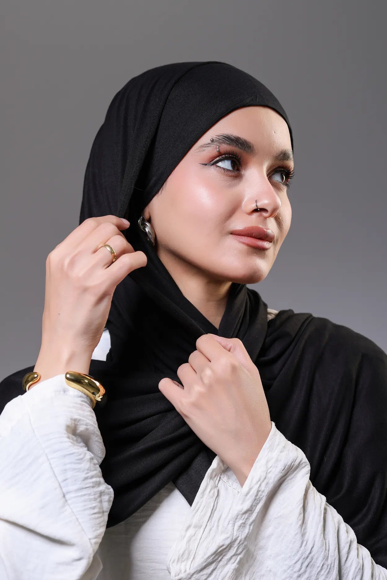 Woman wearing a black hijab against a gray background